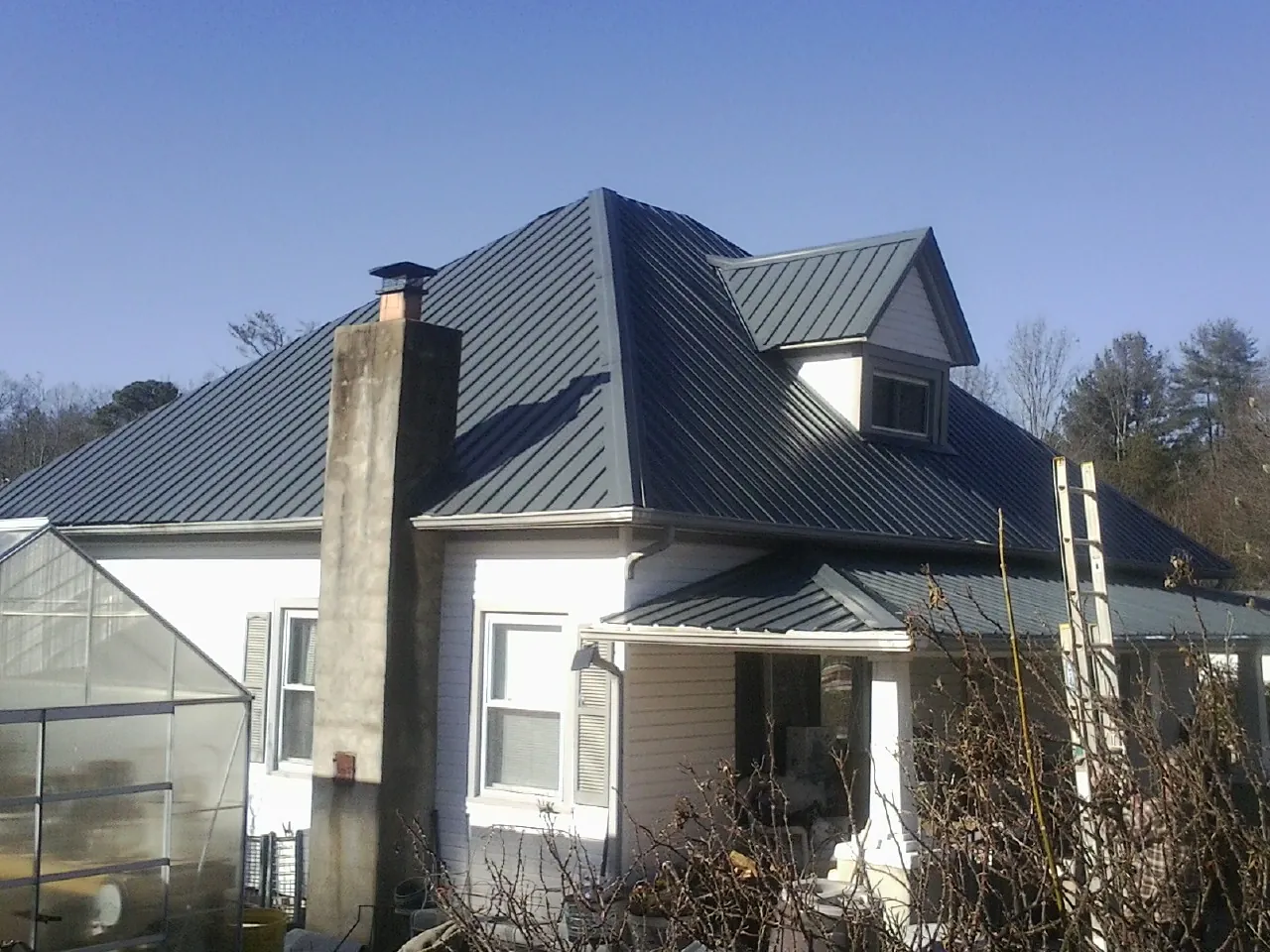 Dark blue standing seam metal roof on a white farmhouse with dormer — Slate & Tile Roof Repair by Roofing Brothers in Madisonville