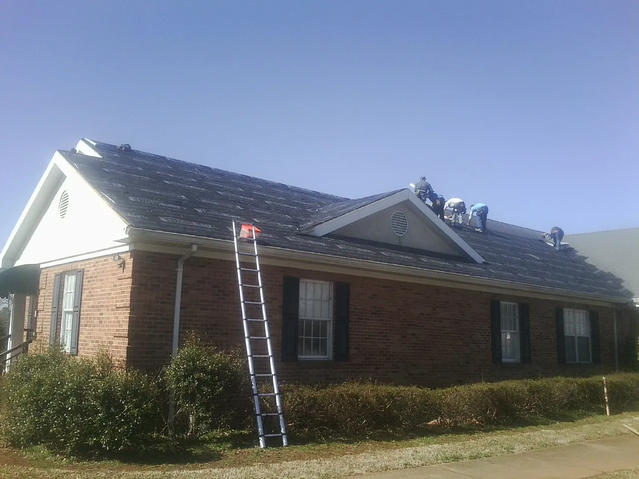 Crew tearing shingles off a brick ranch roof with a ladder set — Emergency Roof Repair work by our crew in Madisonville